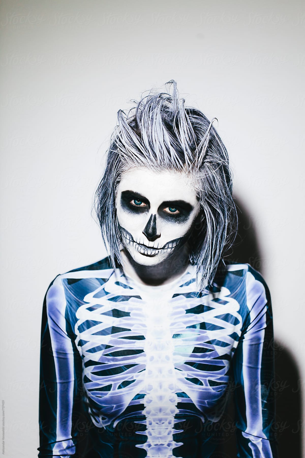Spooky portrait of woman with skeleton costume and halloween make up on white wall