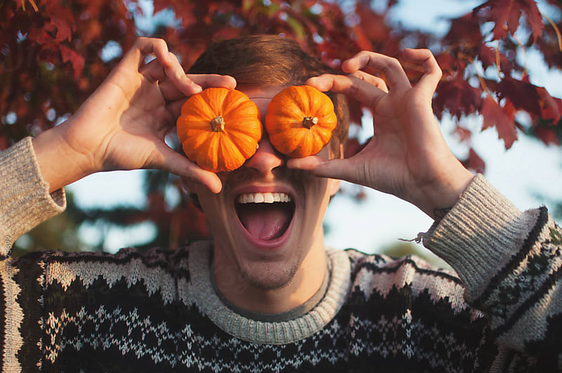 A young man with small pumpkins over his eye making a funny face
