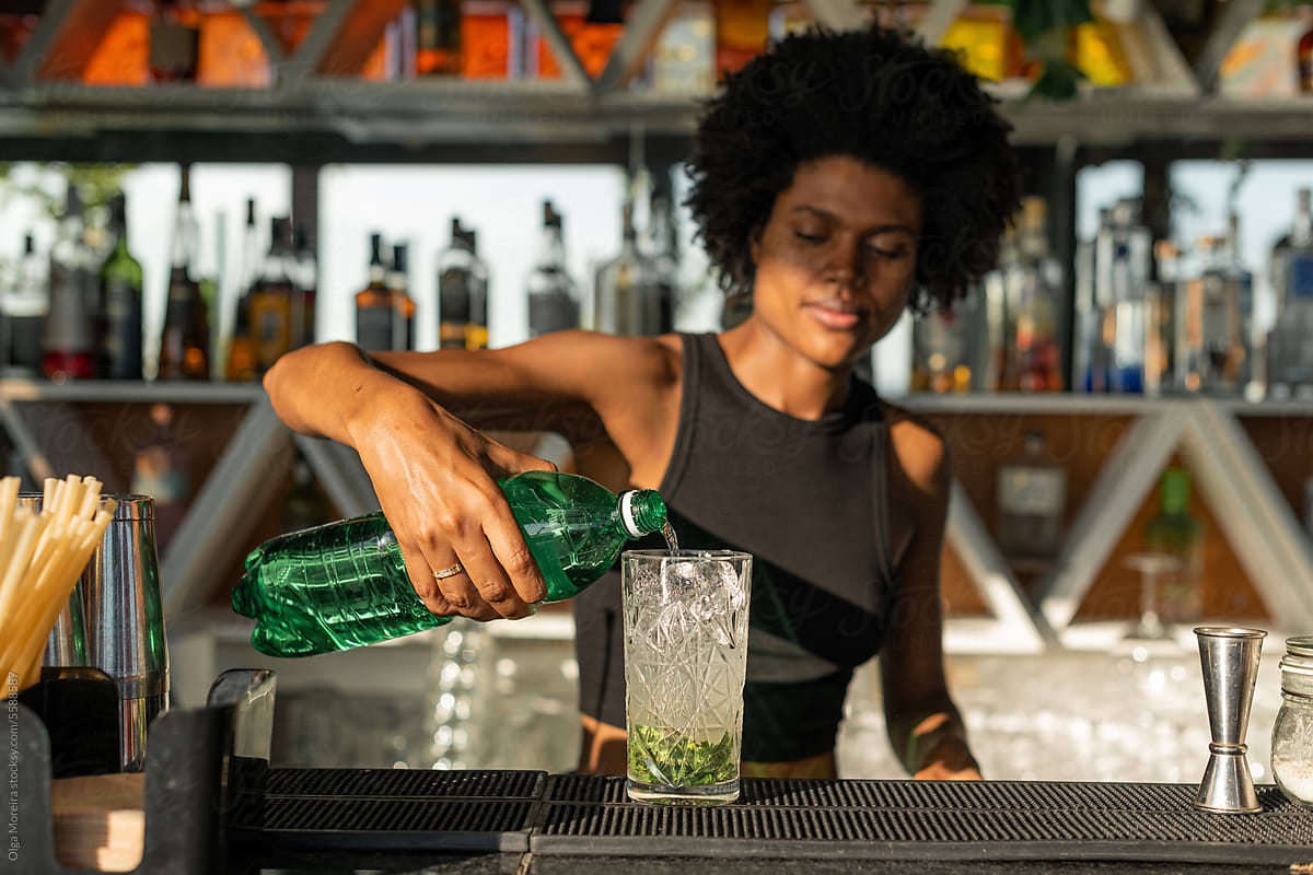 Black female bartender pouring soda water into a glass for mojit