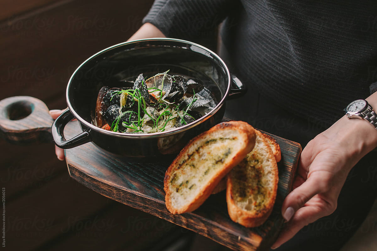 Unrecognizable woman holding plate with mussels and toasted bread