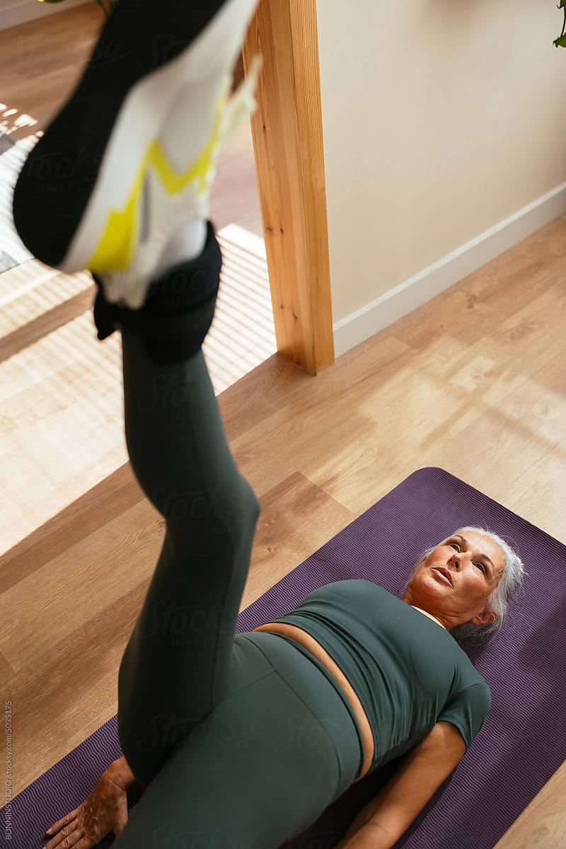Mature woman doing leg rise exercise on purple mat