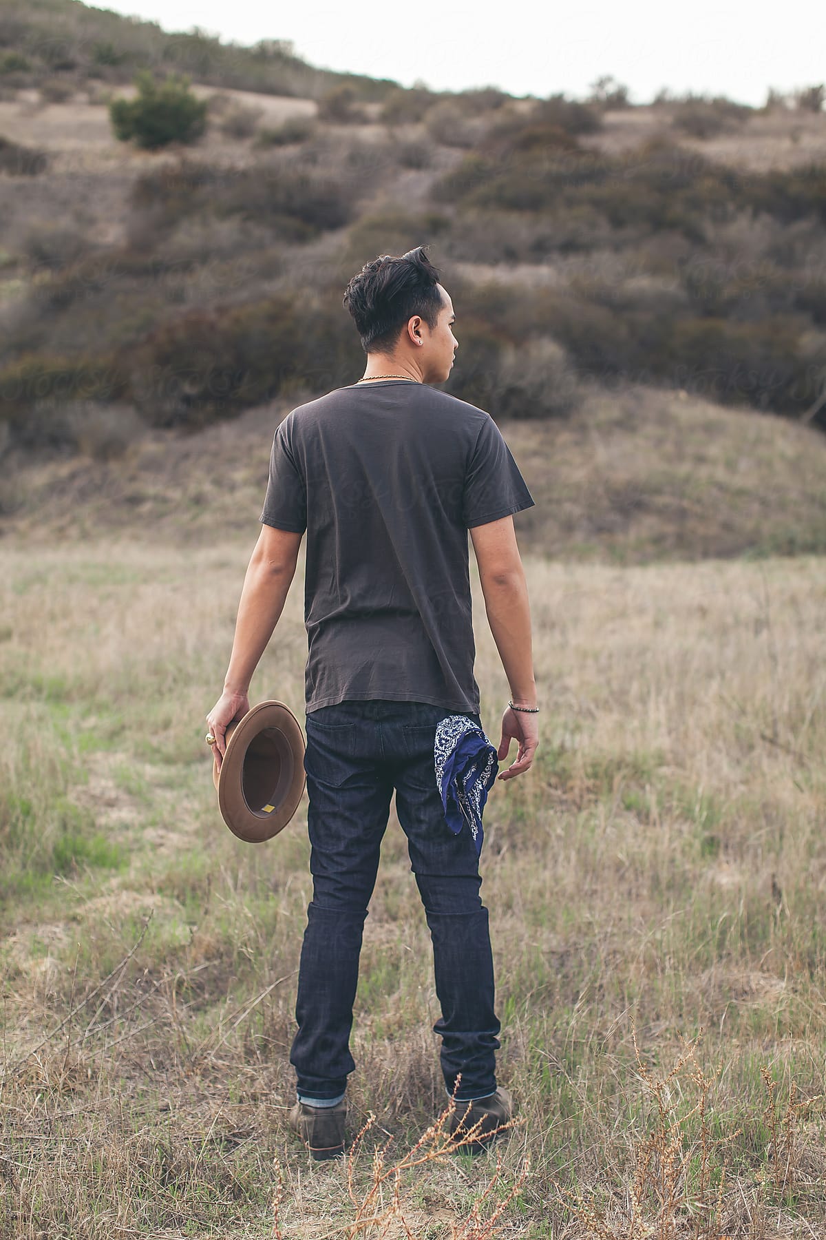 A man wearing jeans a hat walking through an open field.