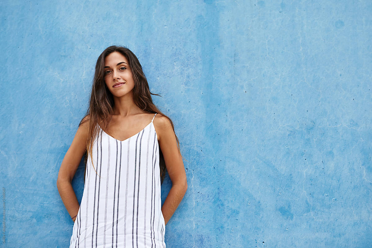 Beautiful girl in striped linen dress over blue wall.