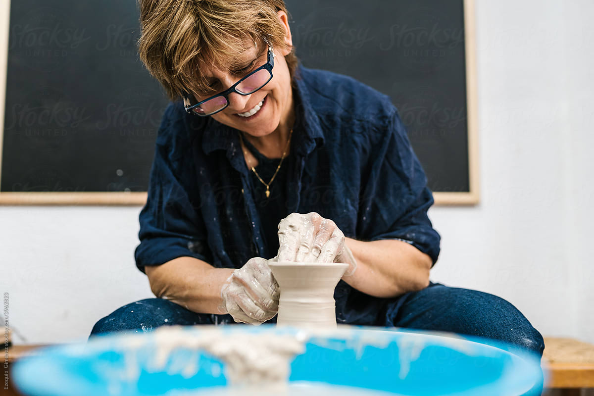 Happy mature potter creating clay vessel