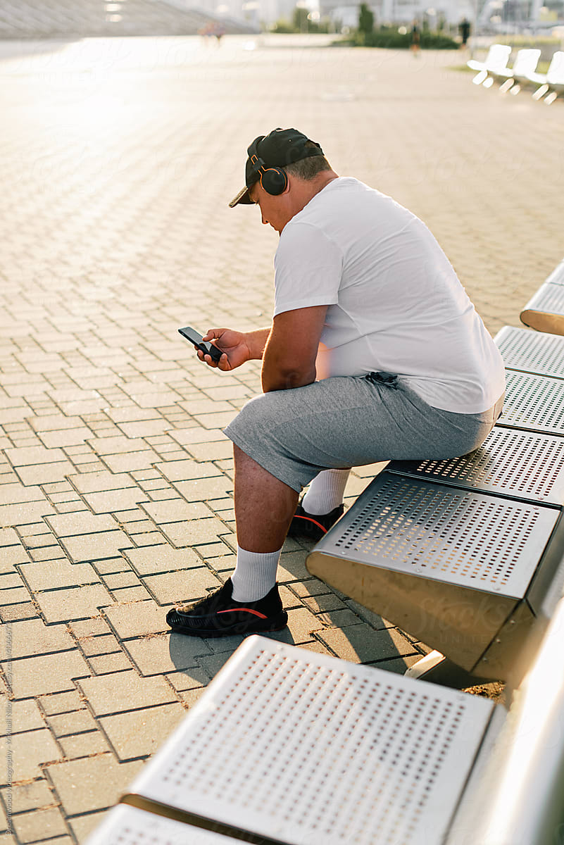 Fat man in sportswear sits on a bench