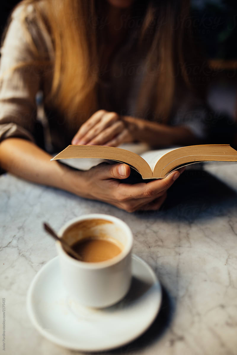 Woman spending time in a cafeteria with phone, coffee and books.