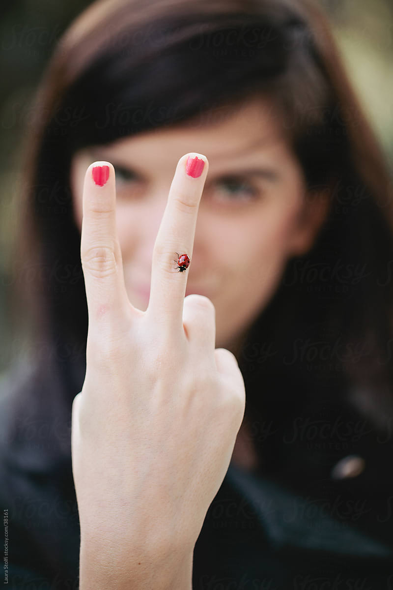 Girl showing the win sign with a ladybug on her finger
