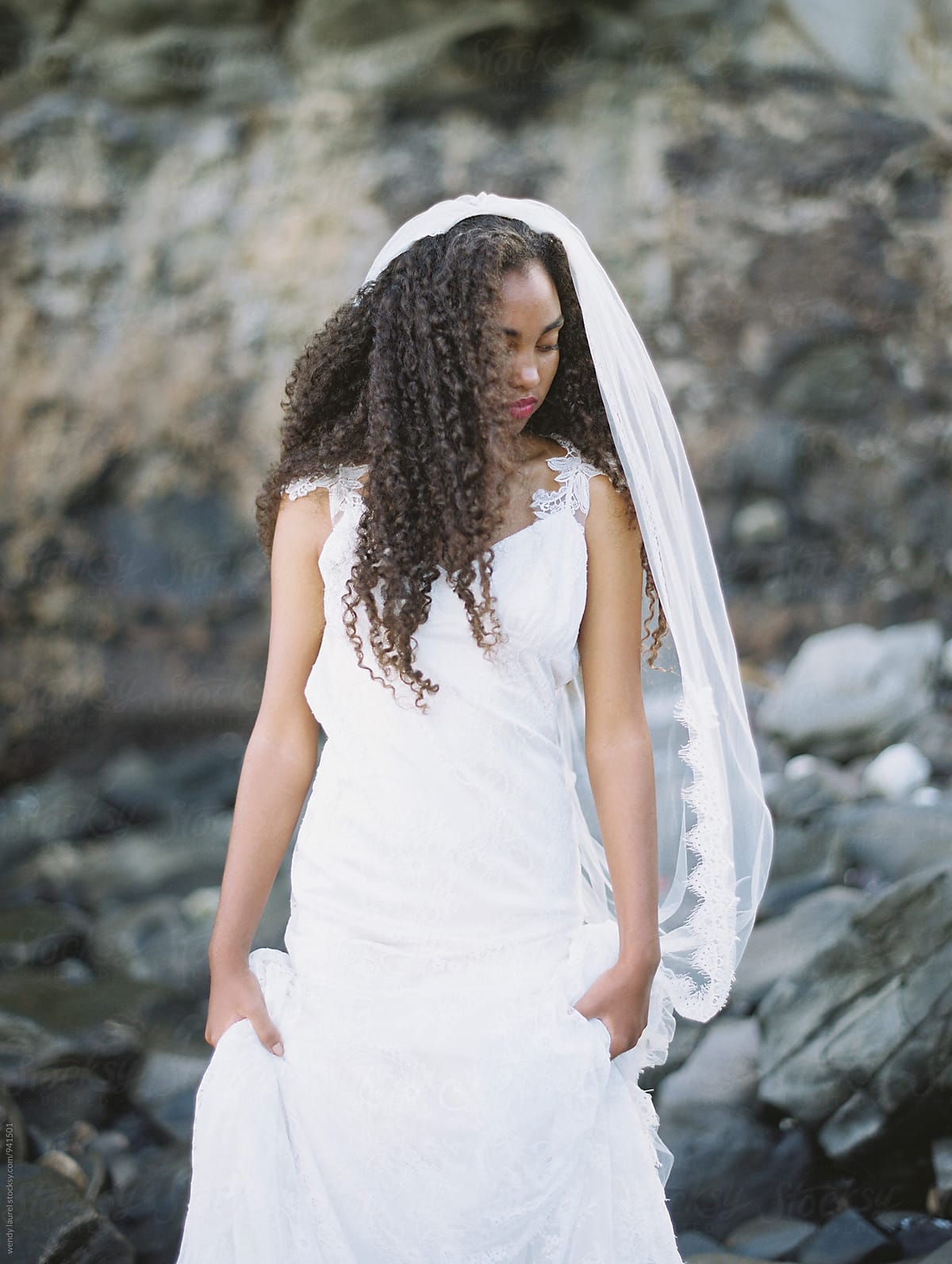 beautiful black bride on beach in gorgeous wedding gown with rocks and ocean