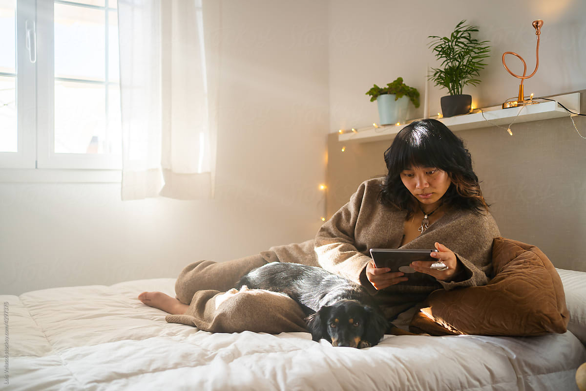 Dog And Asian Girl With Tablet Laying On The Bed.