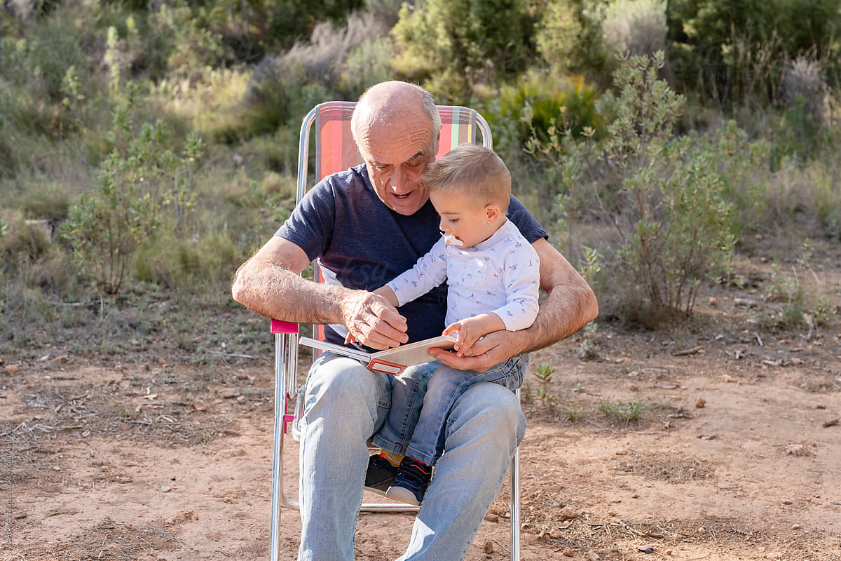 Grandfather reading book with cute kid in nature