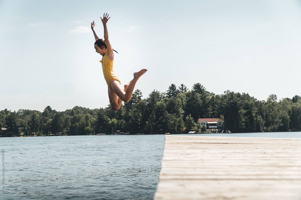 Young girl jumping off dock into a lake in a yellow swimsuit
