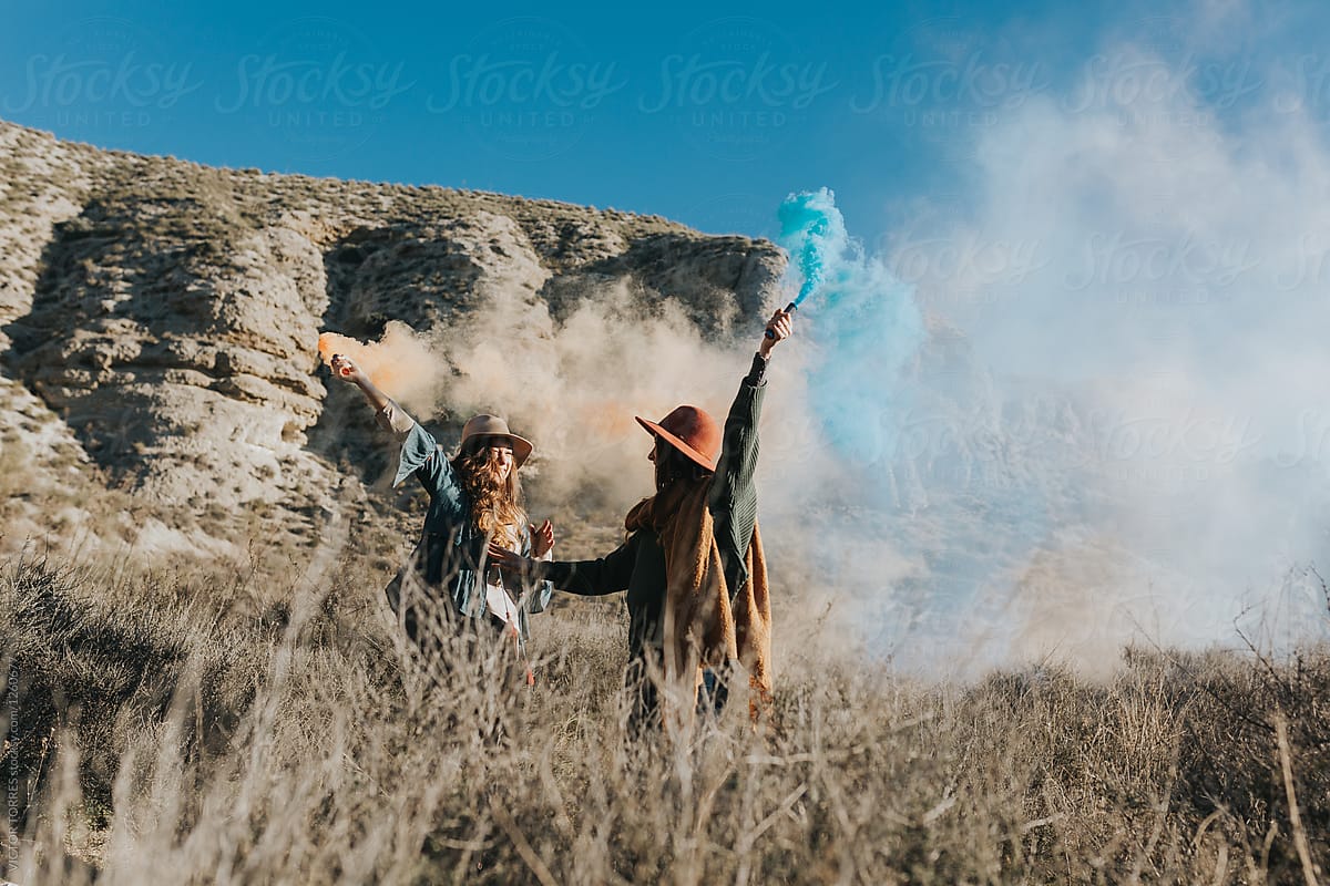 Cheerful teenagers playing with color smoke bombs in the countryside