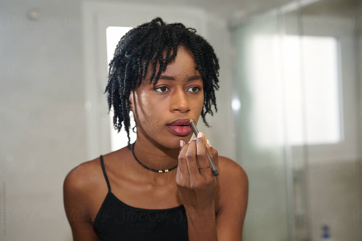 Afro woman applying lipstick