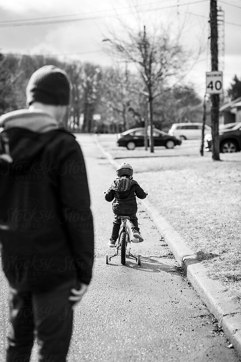 A young boy out for a bike ride with his father in a suburban neighbourhood.
