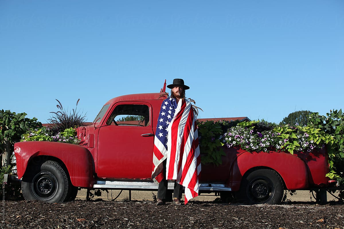 Americana Portrait Of A Cowboy Infront Of A Vintage Truck Wrapped In An American Flag