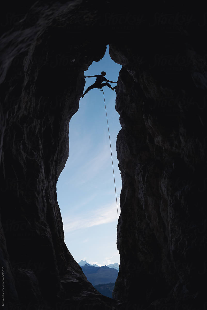 Silhouette of a rock climber climbing the cave entrance