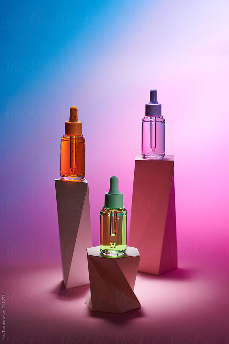 Glass bottles with serum, essential oil on wooden geometric podium