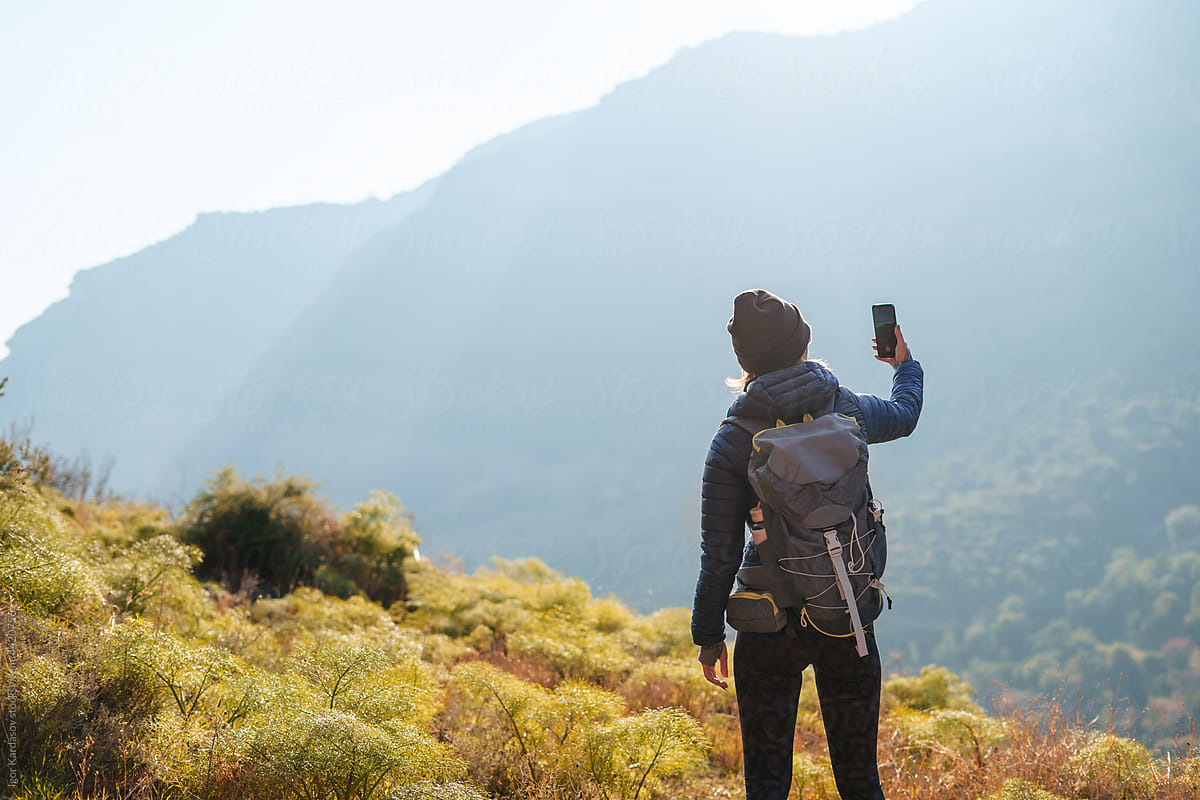 Female hiker taking photo of mountains on smartphone