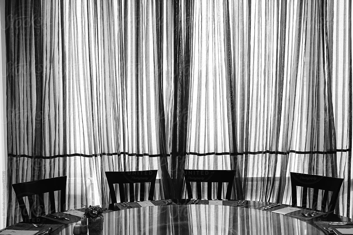 Silhouette image of chairs on a round table and curtain with line patterns in black and white