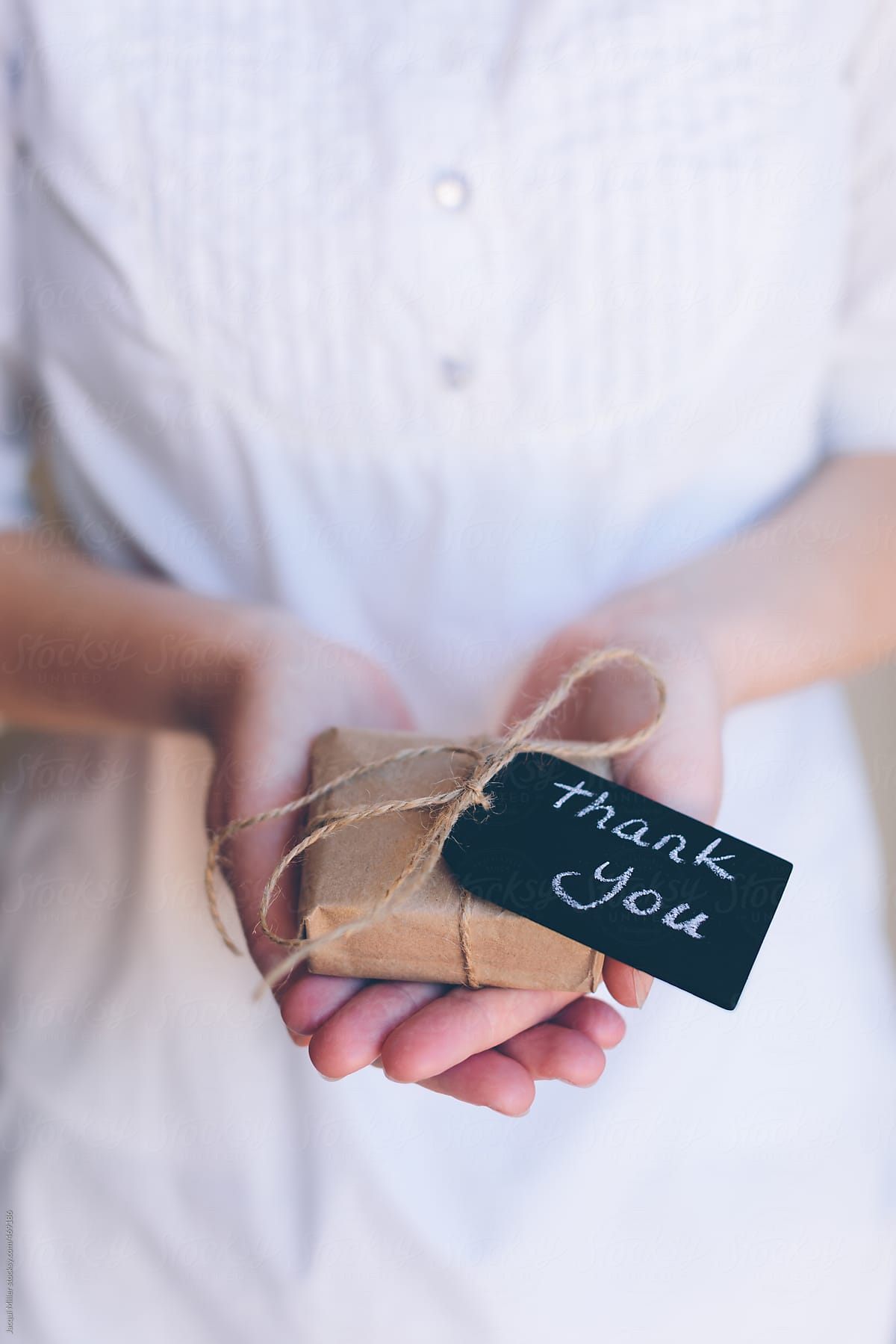 Girls hands holding a small gift with a tag that says \'thank you\'