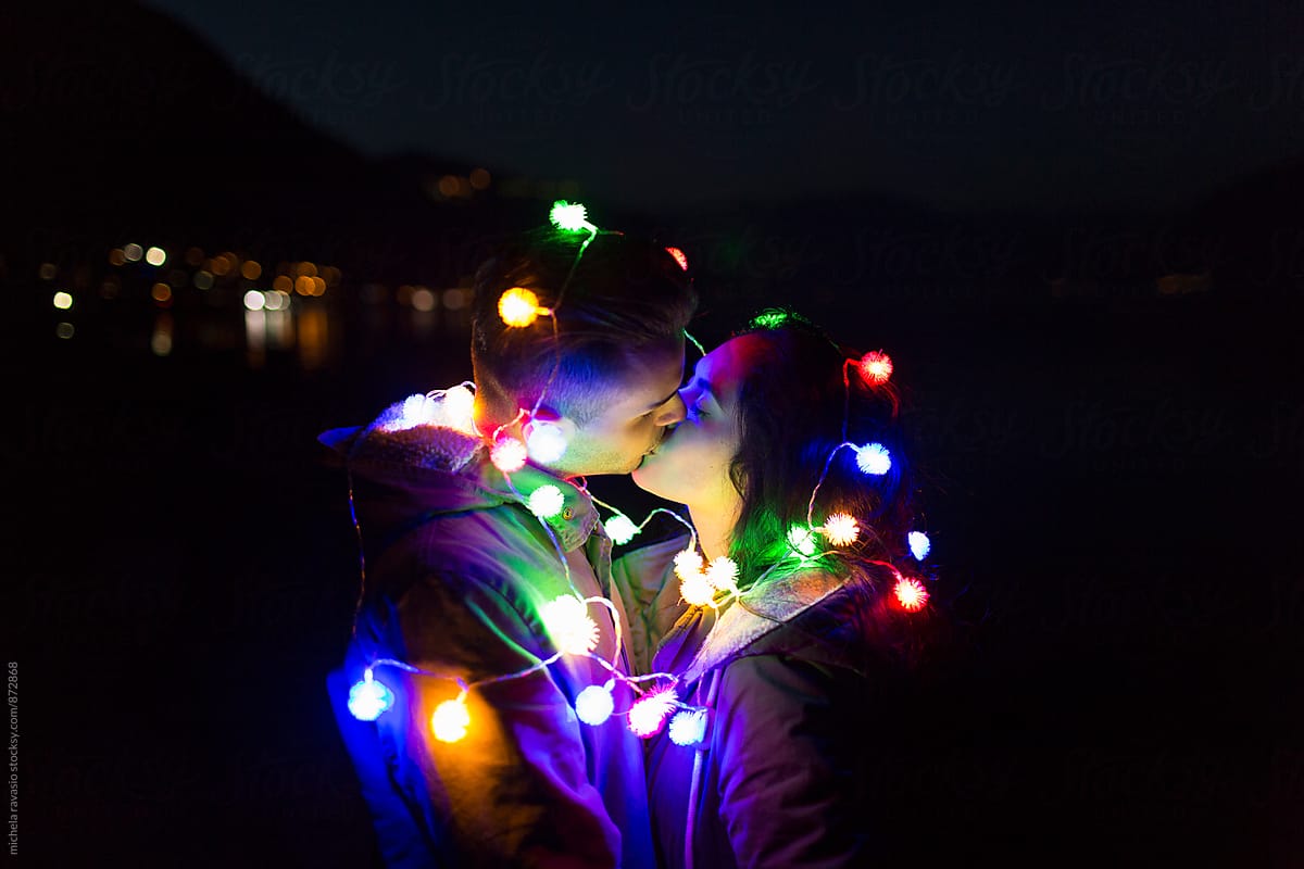 Loving couple kissing in the night lit by colored lights