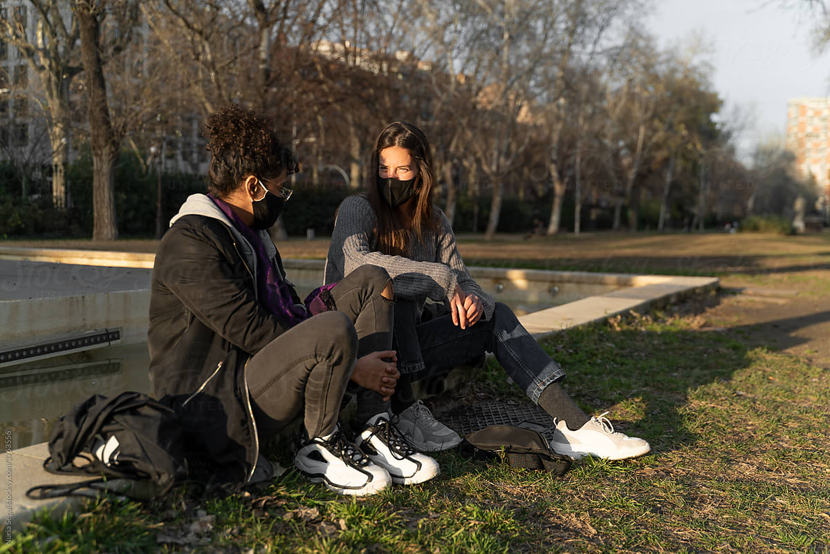 Two young woman talking sitting in a park