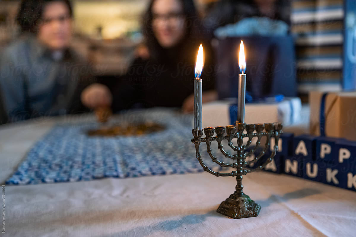 Hanukkah: Menorah With Family Playing Dreidel In Background