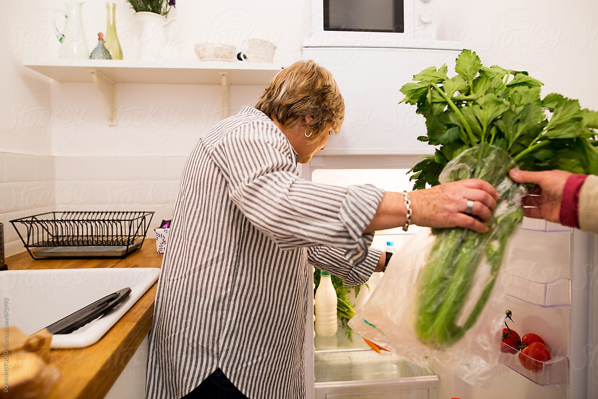 Elderly woman putting organic food into the fridge.