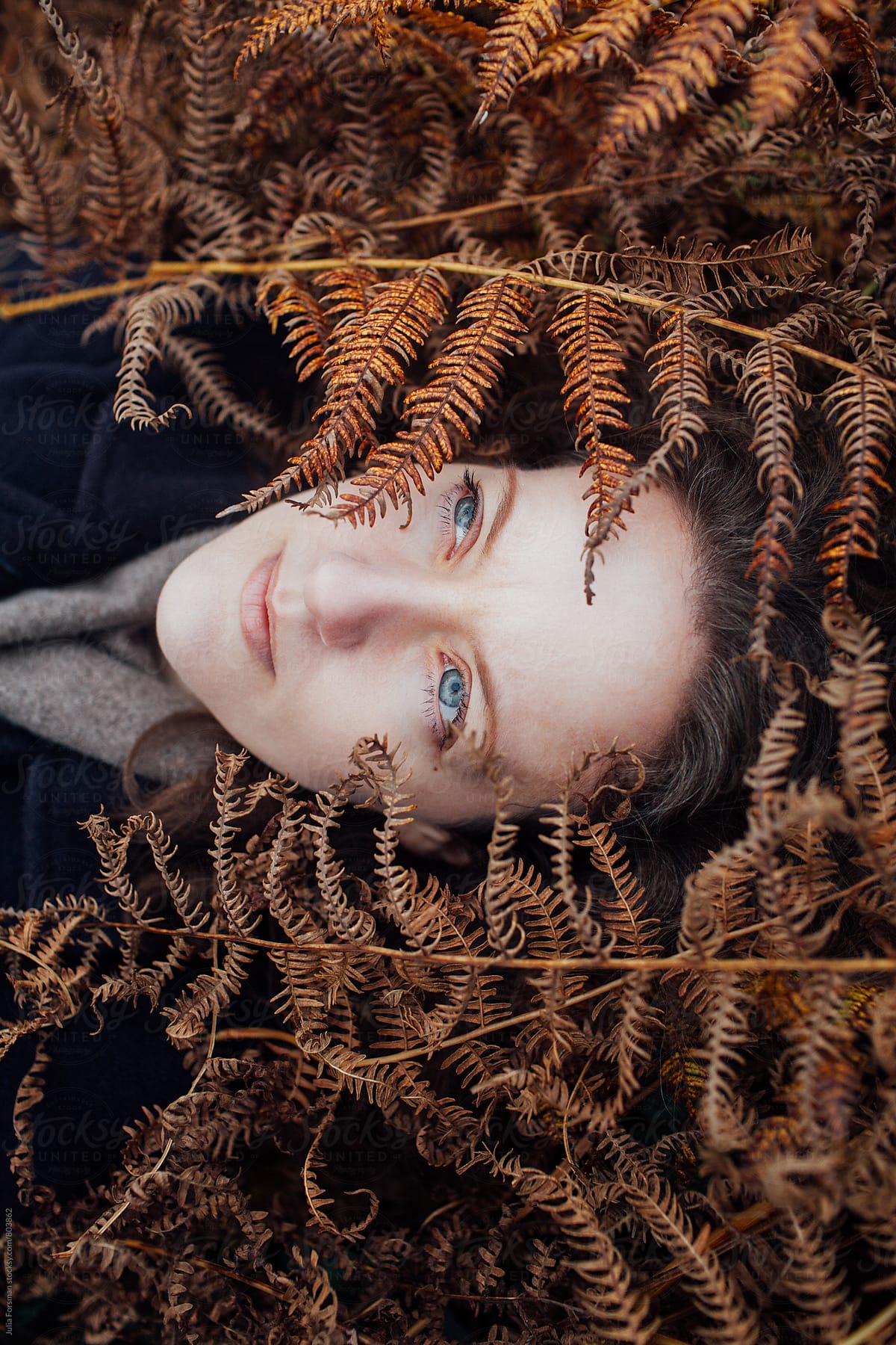 A pale woman with blue eyes lies in golden ferns.