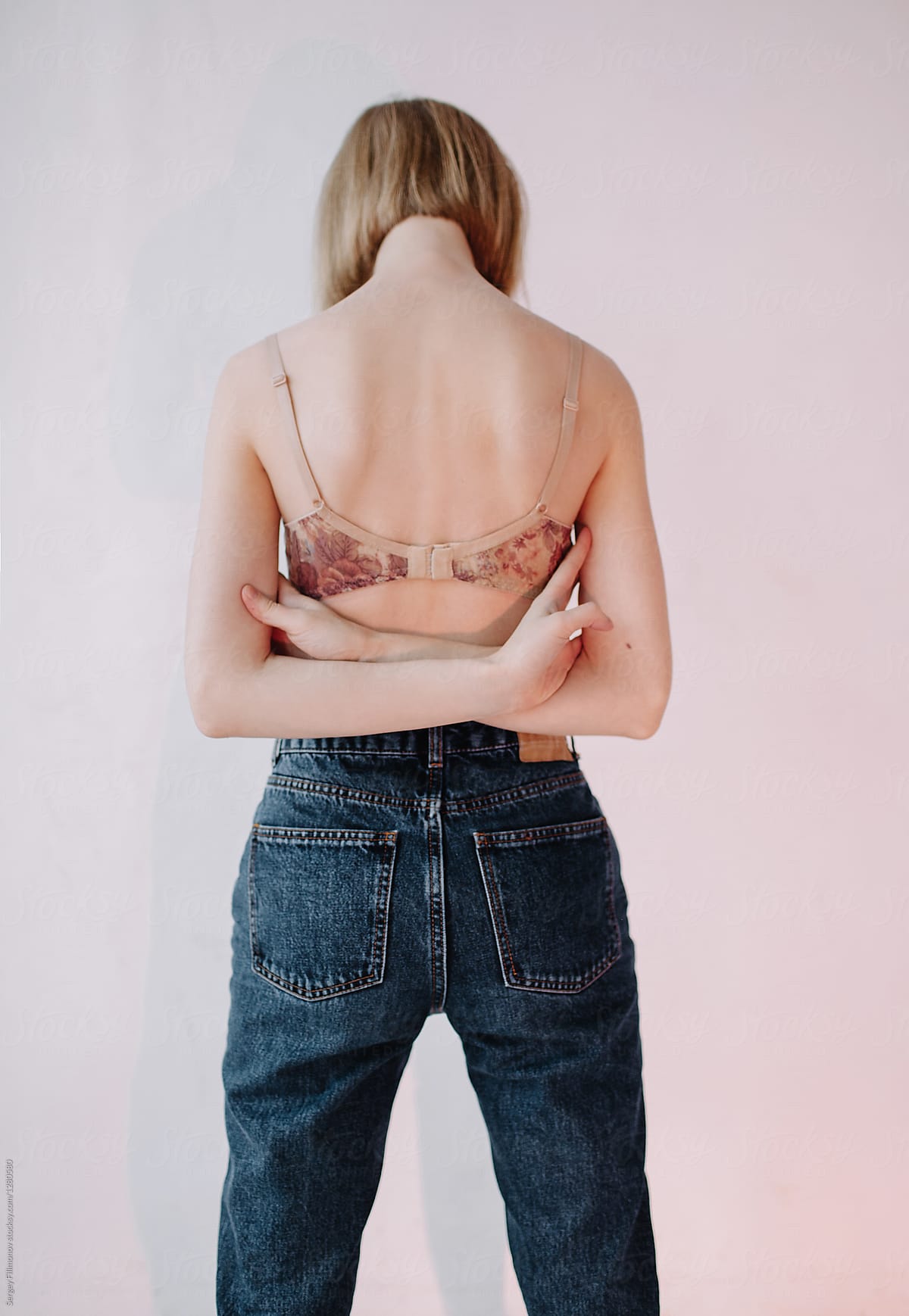 Back view of blonde girl in lingerie and jeans on a color background