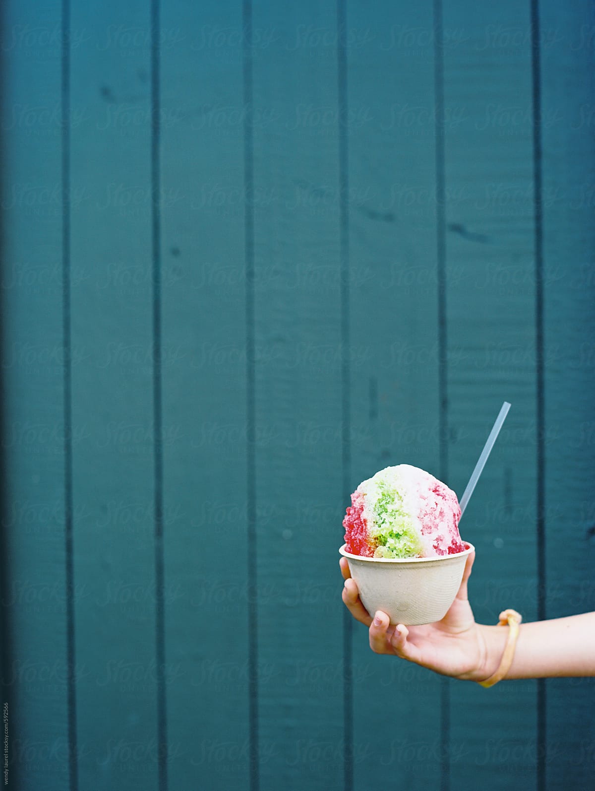 rainbow shave ice held in front of blue wall