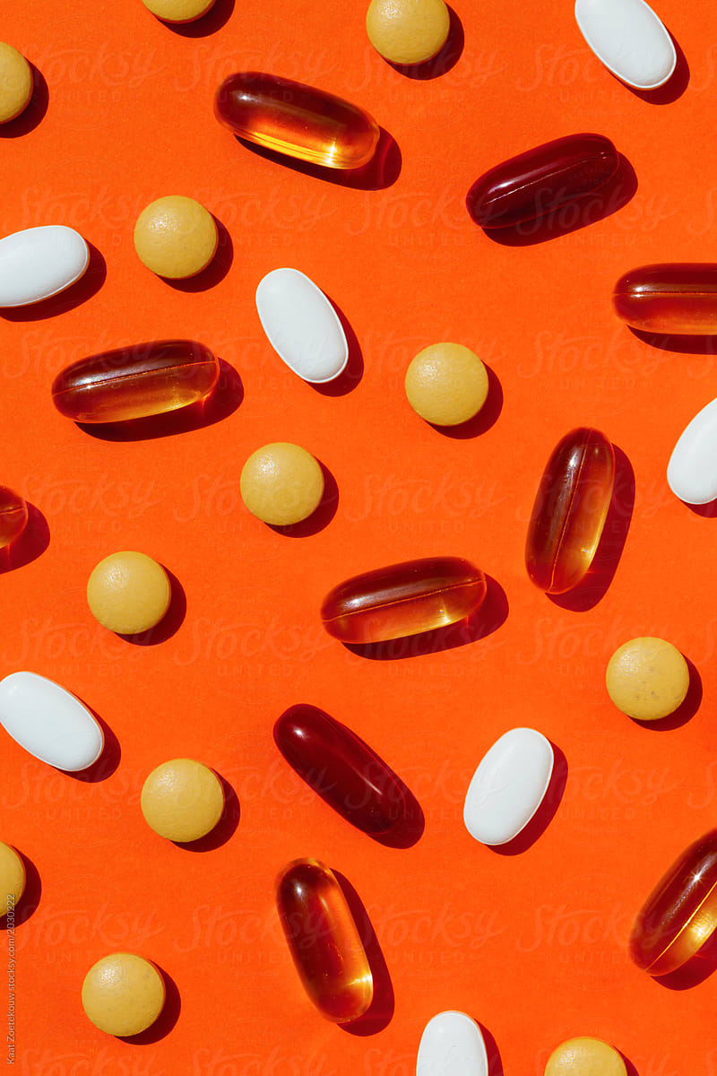 Scattered vitamins and fish oil capsules on an orange background
