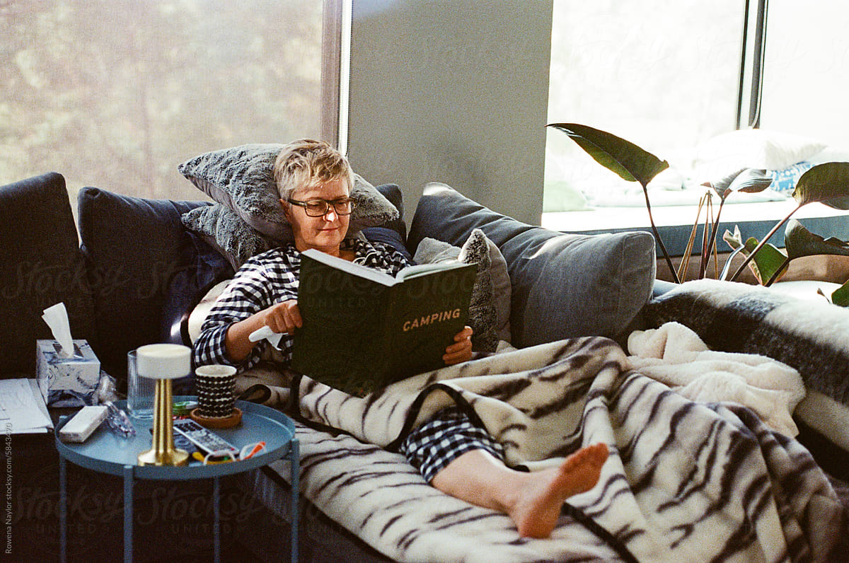Woman sick at on the couch reading book