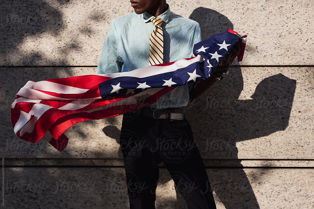 Black businessman holding a american flag. Copyspace on wall