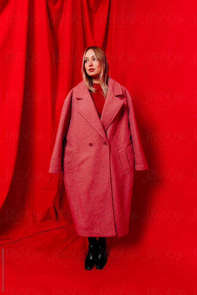 Young woman in stylish red coat standing in studio