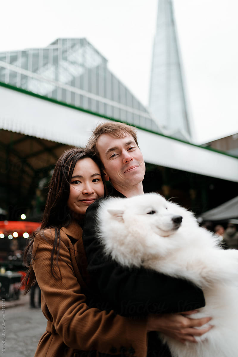 A serene couple holds their dog and looks at the camera for a photo