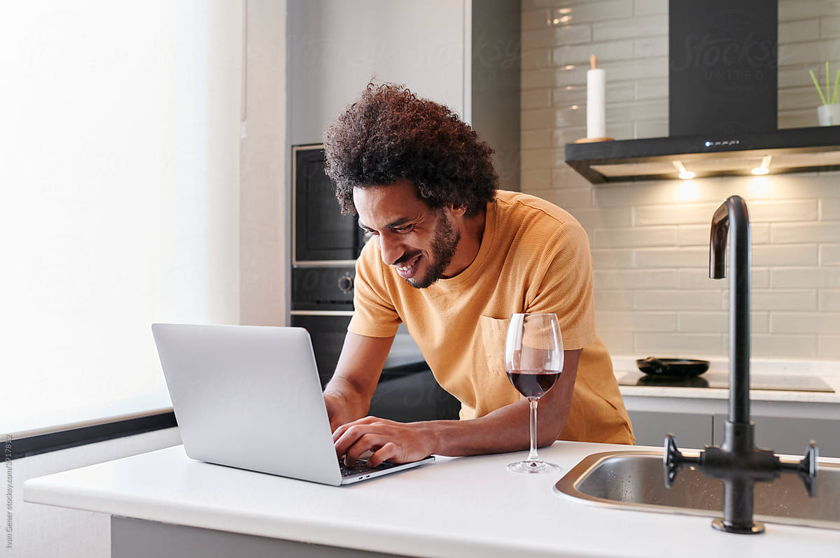 Smiling man using a laptop and drinking wine