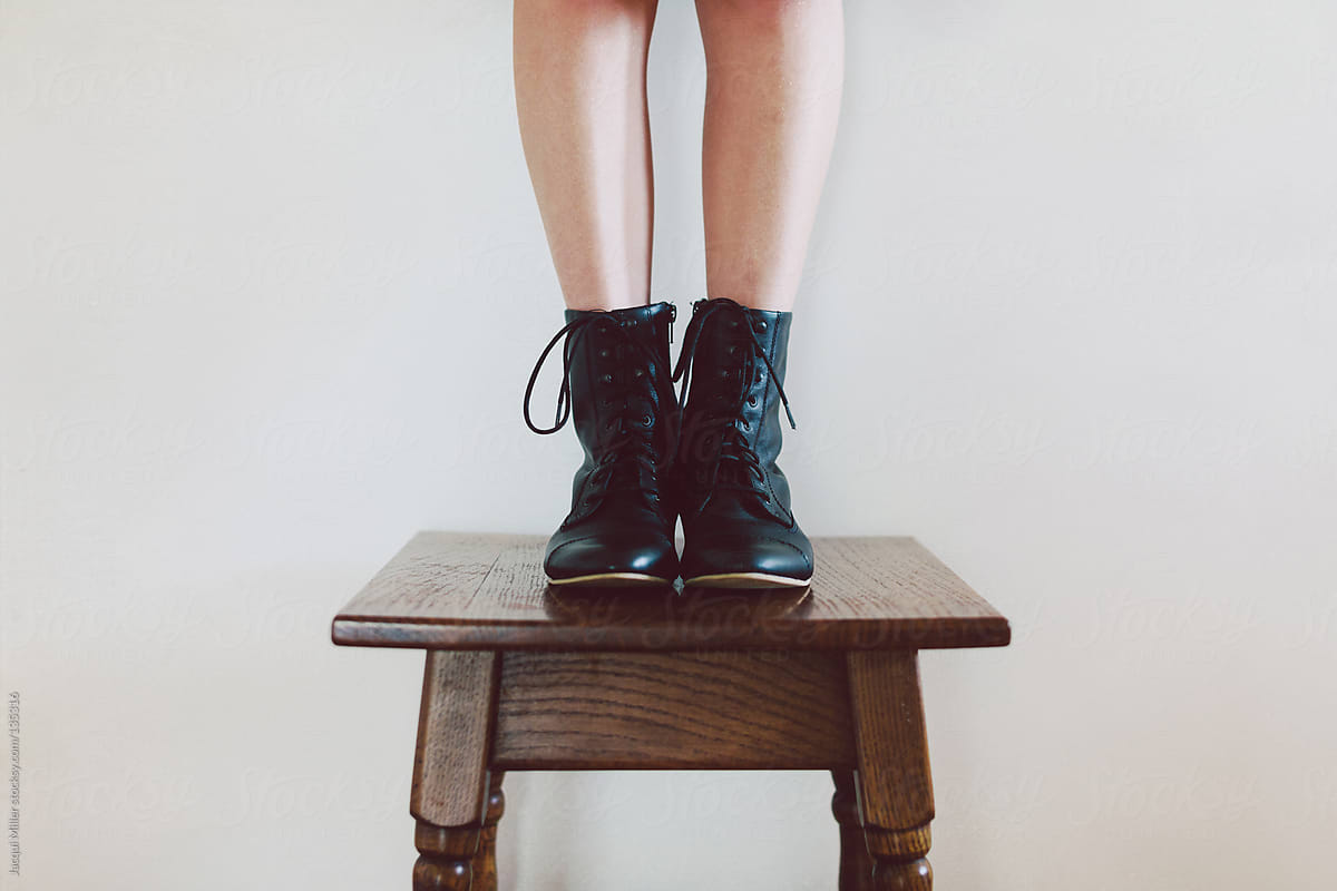 Girl wearing black lace up boots stands on an antique table.