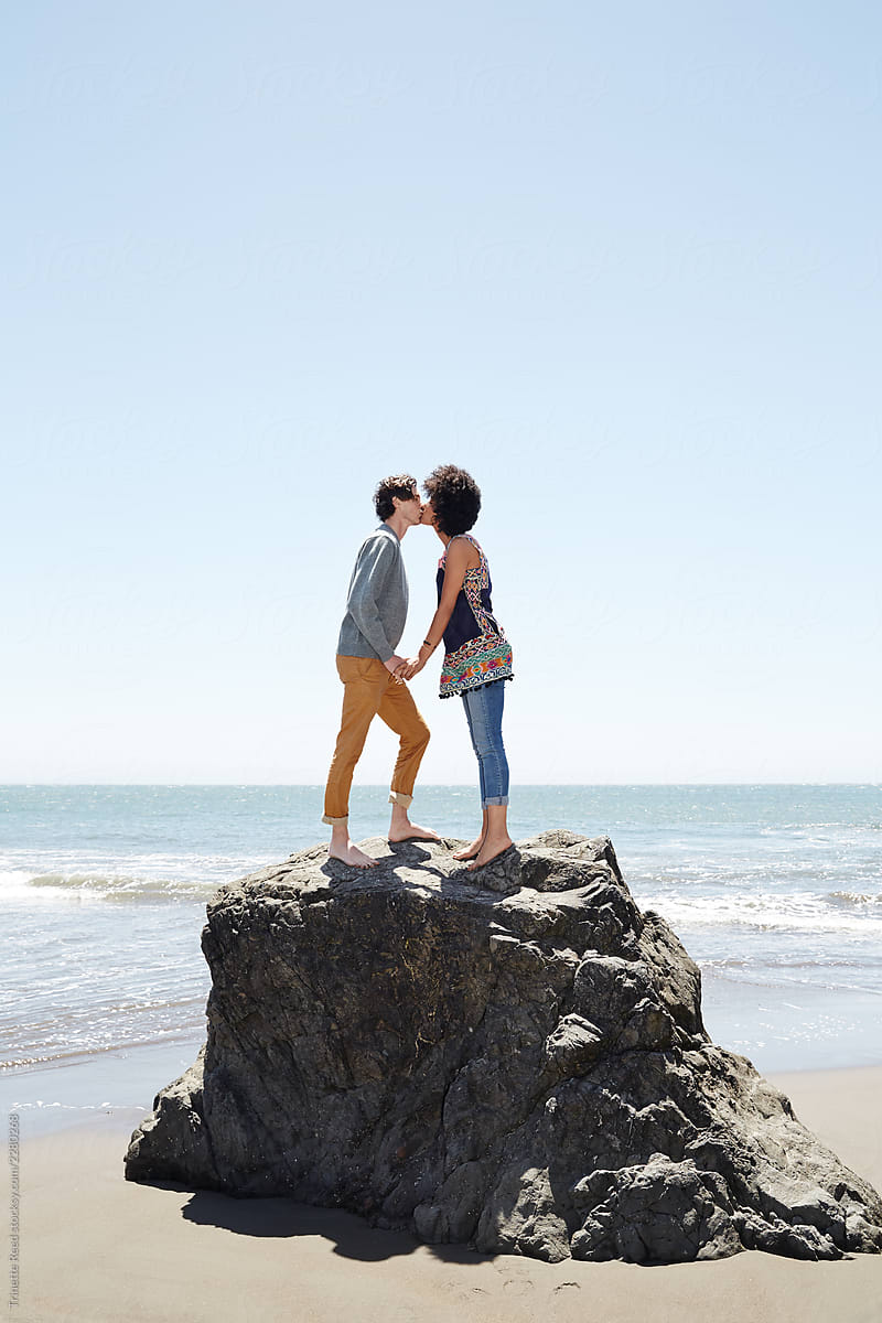 Couple Standing On Top Of A Rock On The Beach Kissing By Stocksy