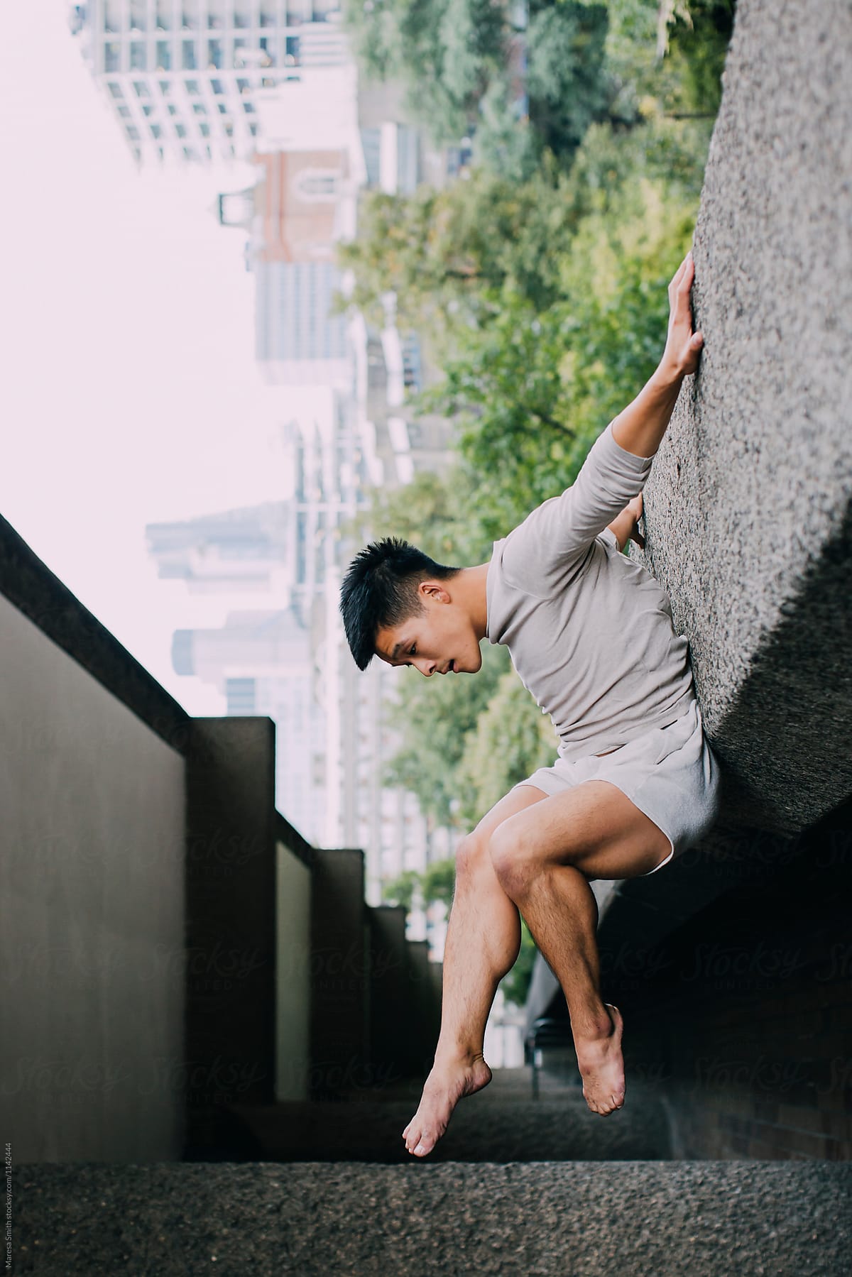 An asian man appears to be hanging from a concrete ledge in an urban location