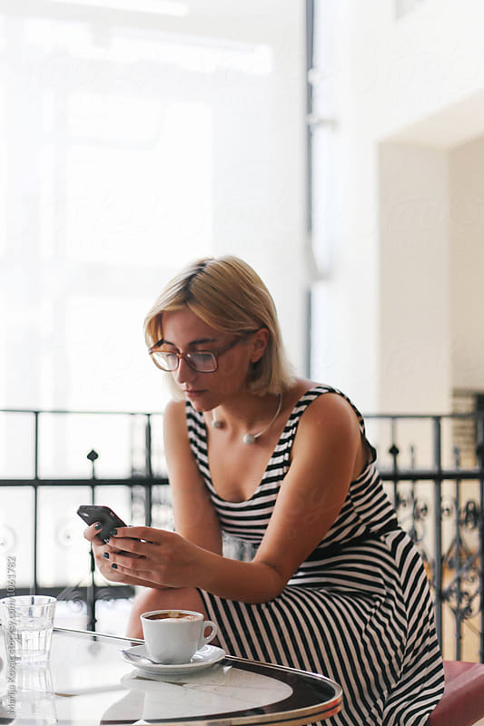 Blonde woman sitting in a coffee shop and browsing on her mobile phone