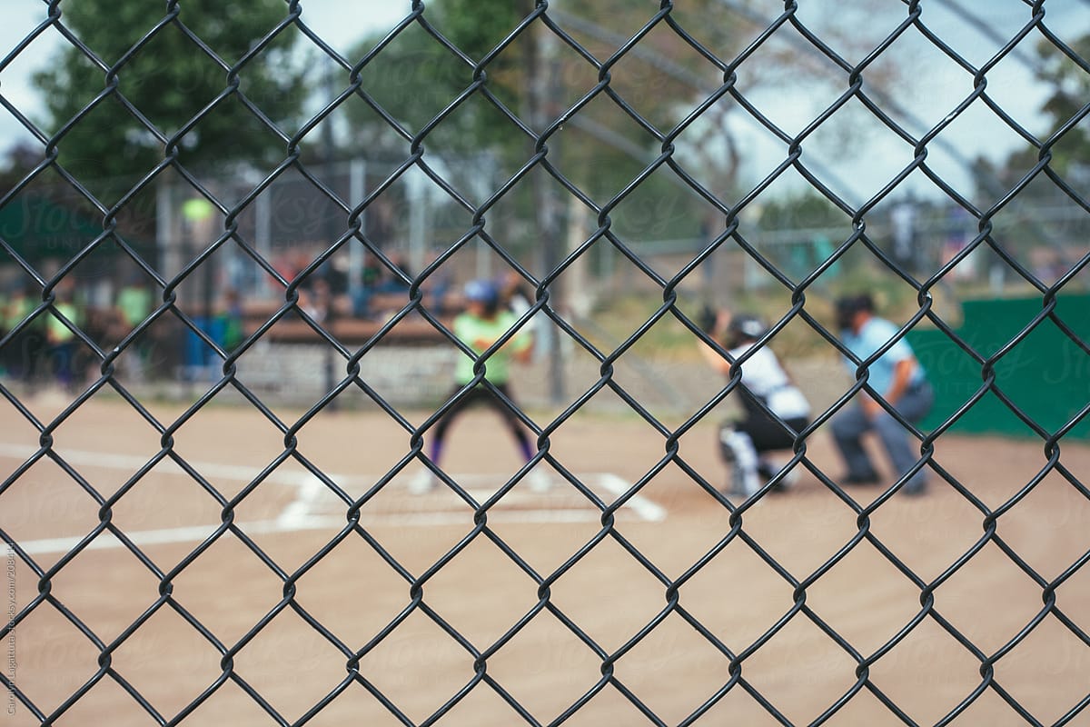 Girl\'s softball game - fence in focus, batter, catcher and umpire blurred