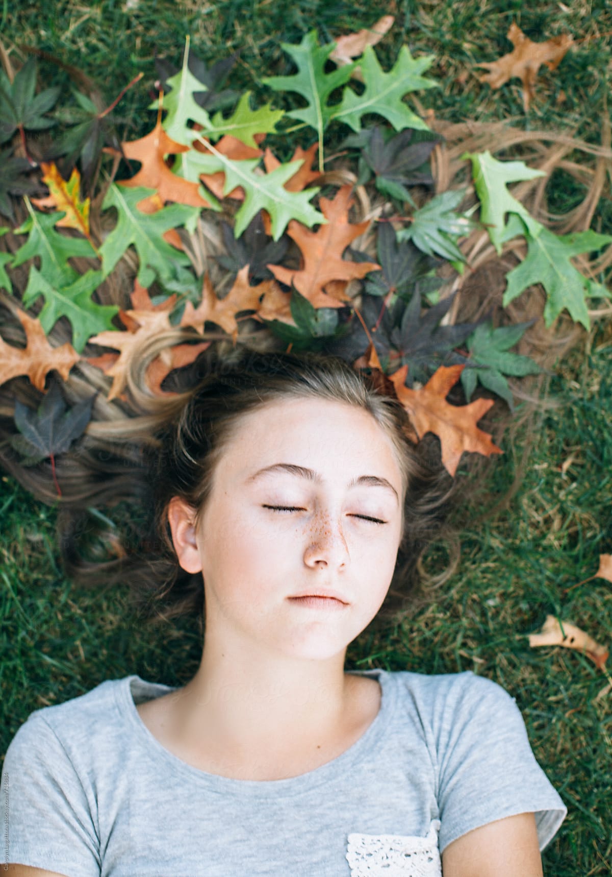 Teenage Girl Laying In The Grass With Her Long Hair Decorated With Fallen Leaves By Stocksy