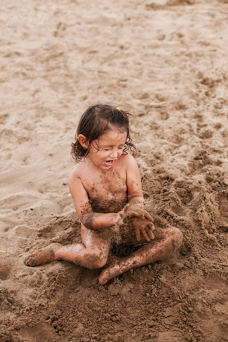 Little girl in green bathing suit plays in sand on beach, green