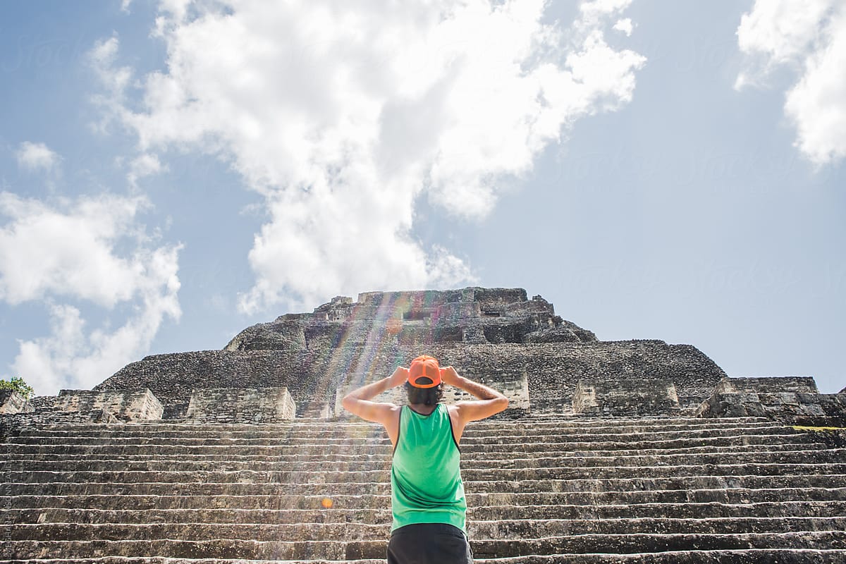 Man Holds His Hat While Looking Up at Ancient Mayan Temple