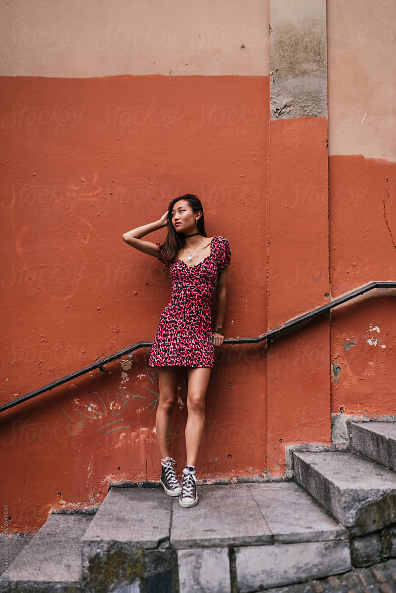 Asian woman posing in a printed red dress and shoes in the stairs.