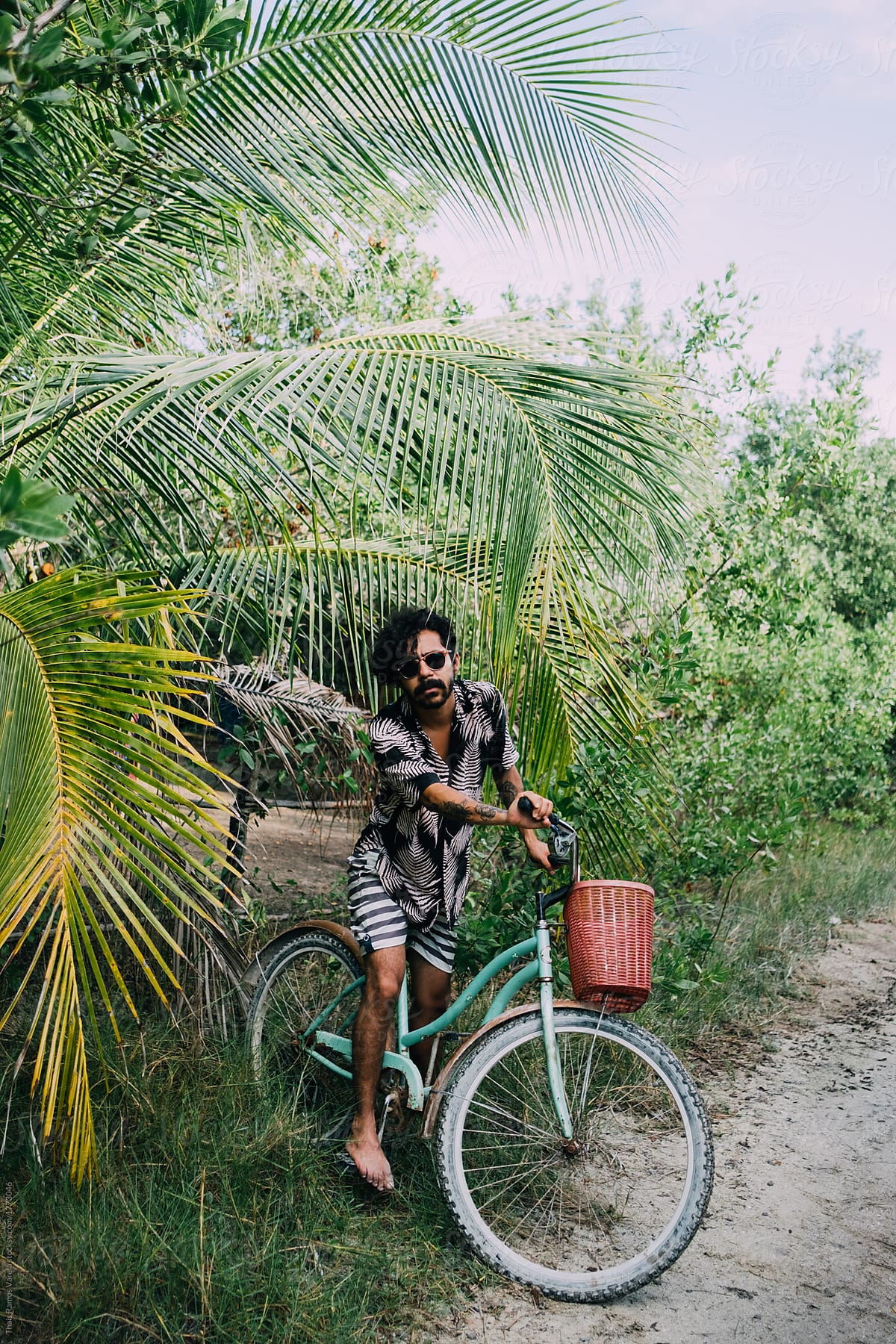 portrait of a cool hispanic man on bicycle among tropical plants