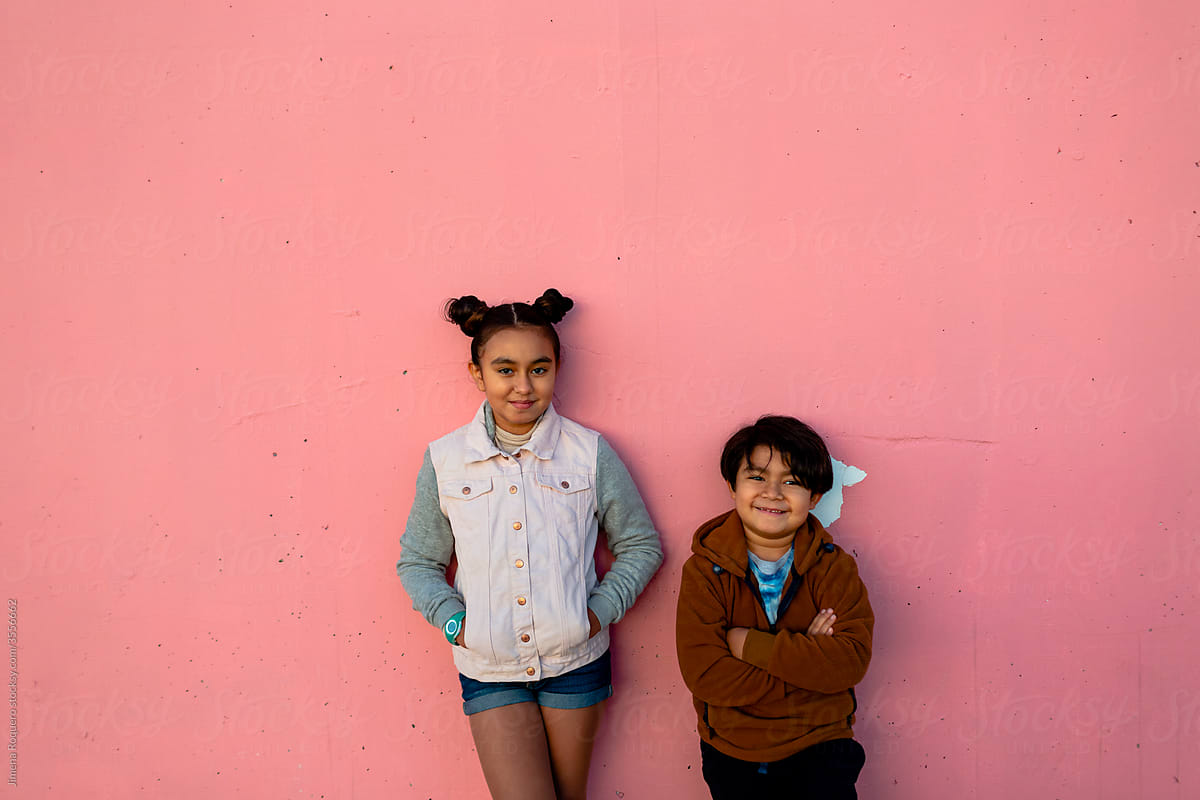 Hispanic Brother and sister posing smiling to camera over pink wall.
