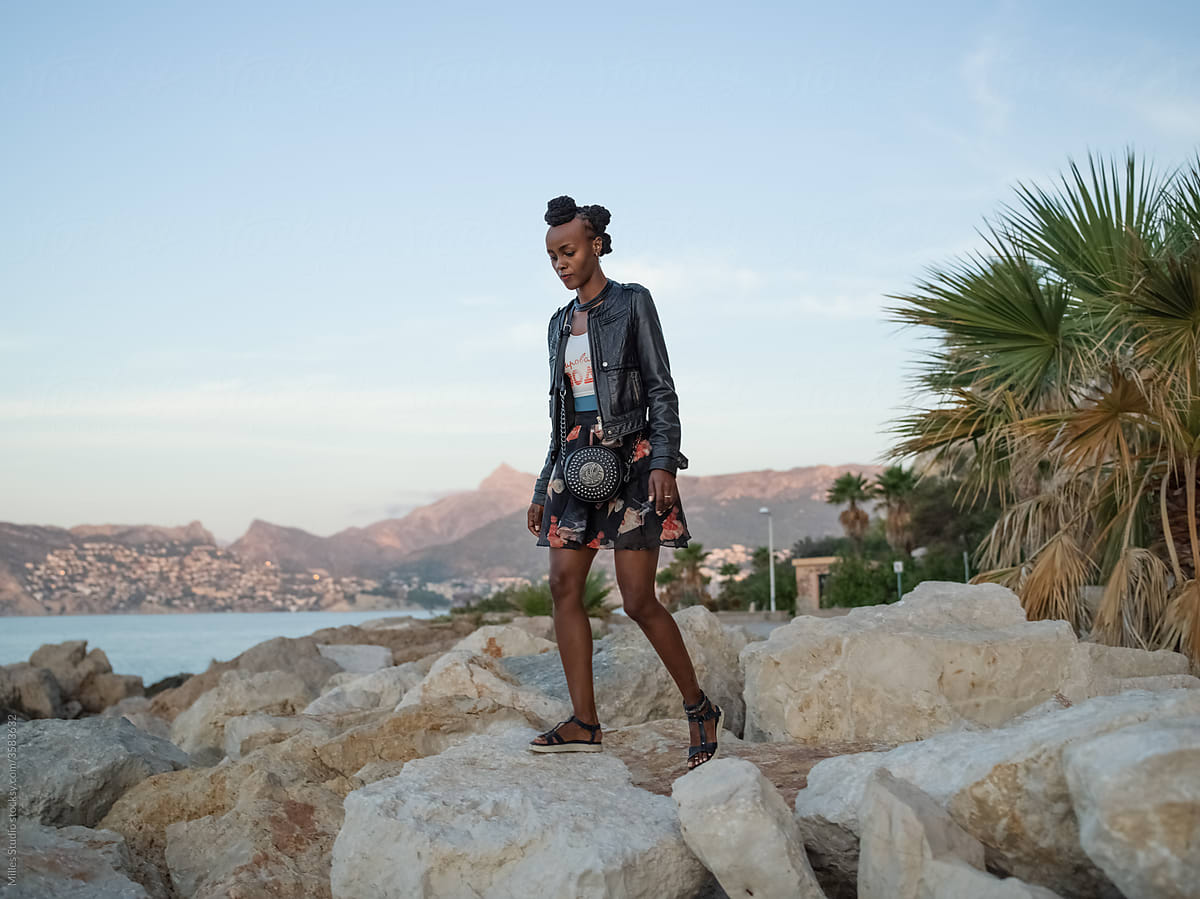 Black woman walking on stones near palm