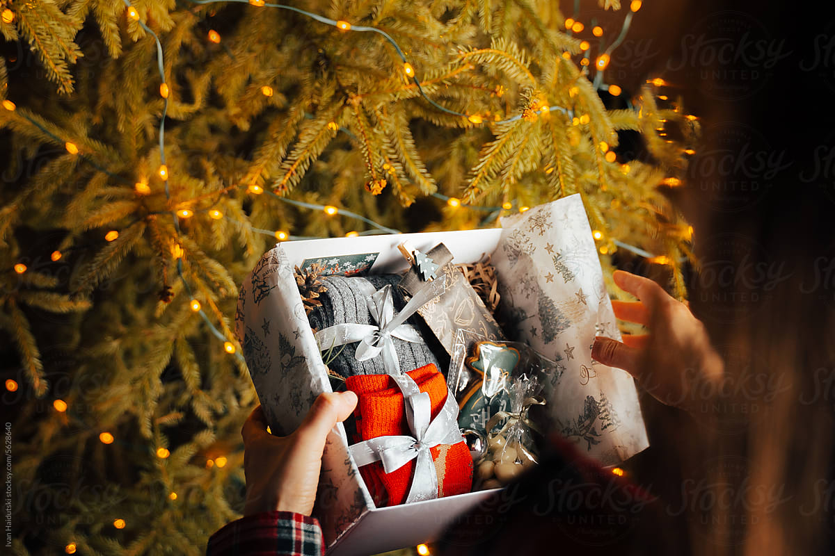 Woman opening Christmas present gift box near the xmas tree at home